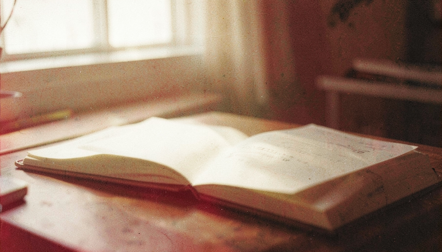 A grainy analog film photograph of an open notebook on a desk, soft window light, muted cream and shadow tones.