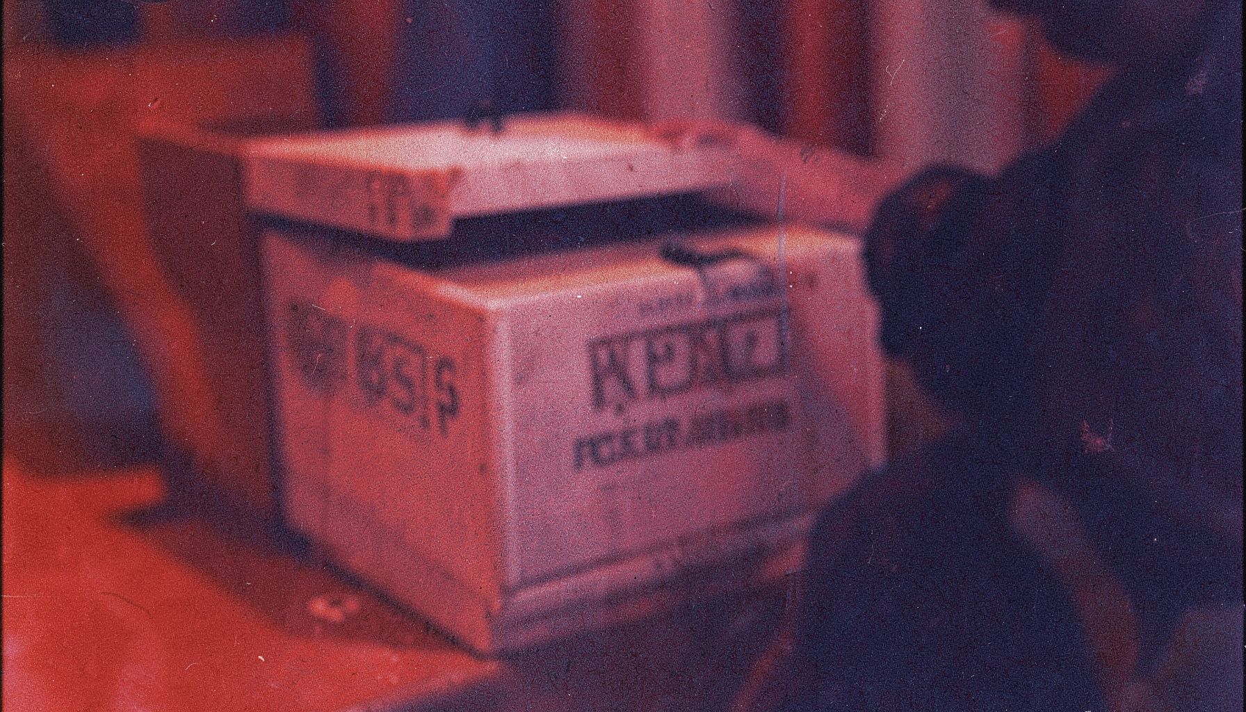 A grainy analog film photograph of a ballot box in soft focus, deep red and navy tones, contemplative political mood.